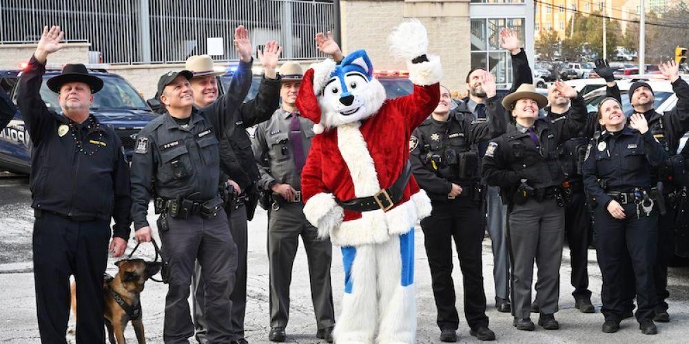 GREETINGS FOR THE KIDS: Officers from more than a dozen law enforcement and first responder agencies, along with Upstate University Police and Upstate’s mascot, Hero, gather Dec. 22 outside Upstate Golisano Children’s Hospital to send holiday wishes to the children, who watched from a top floor of the hospital. The officers arrived in motorcade of emergency vehicles with flashing lights and sirens.